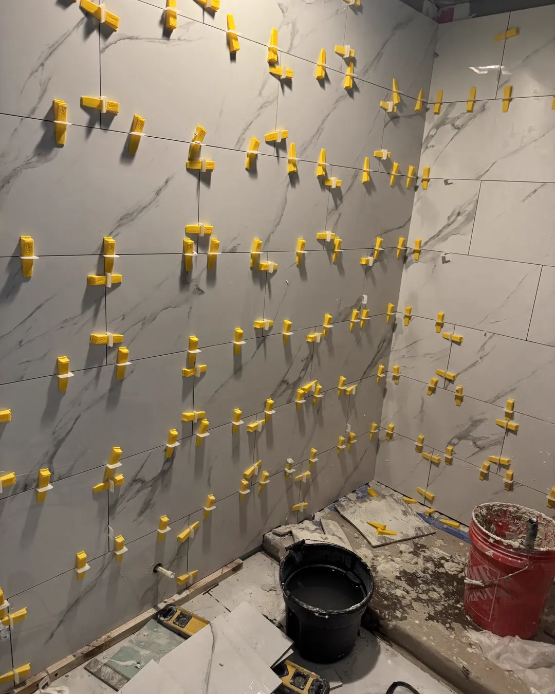 Large format porcelain tile being set on the shower wall over the waterproofed board