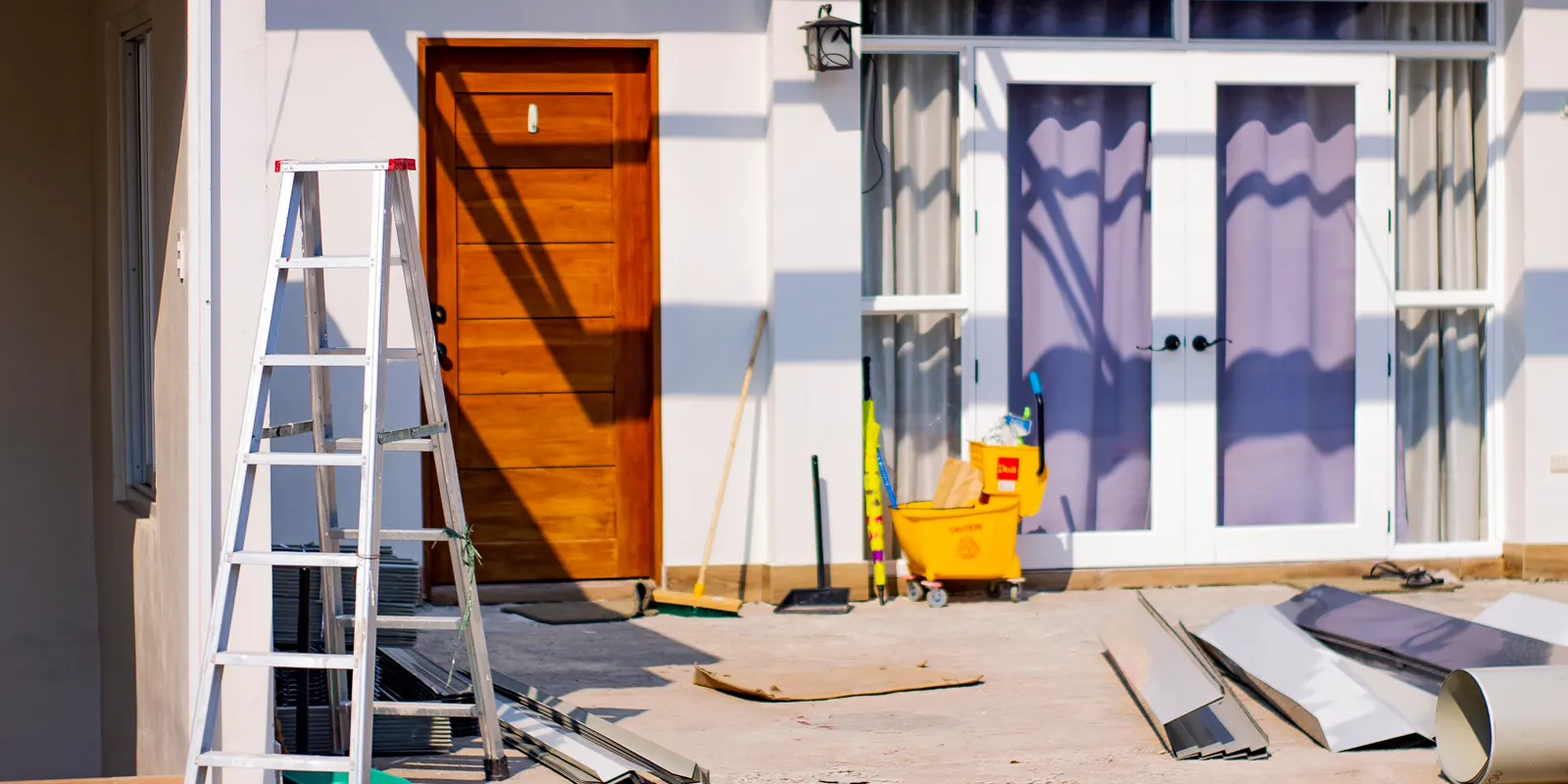 The front entrance of a house mid renovation, with a ladder and paint tools at the door
