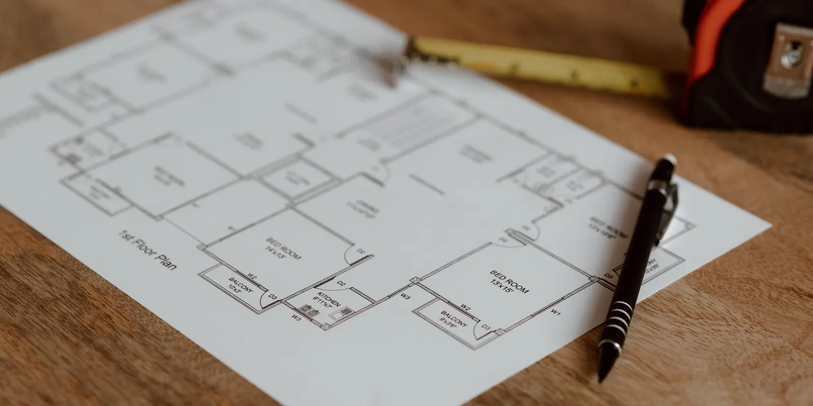 A house floor plan on a wooden surface next to a pen and a ruler during a renovation