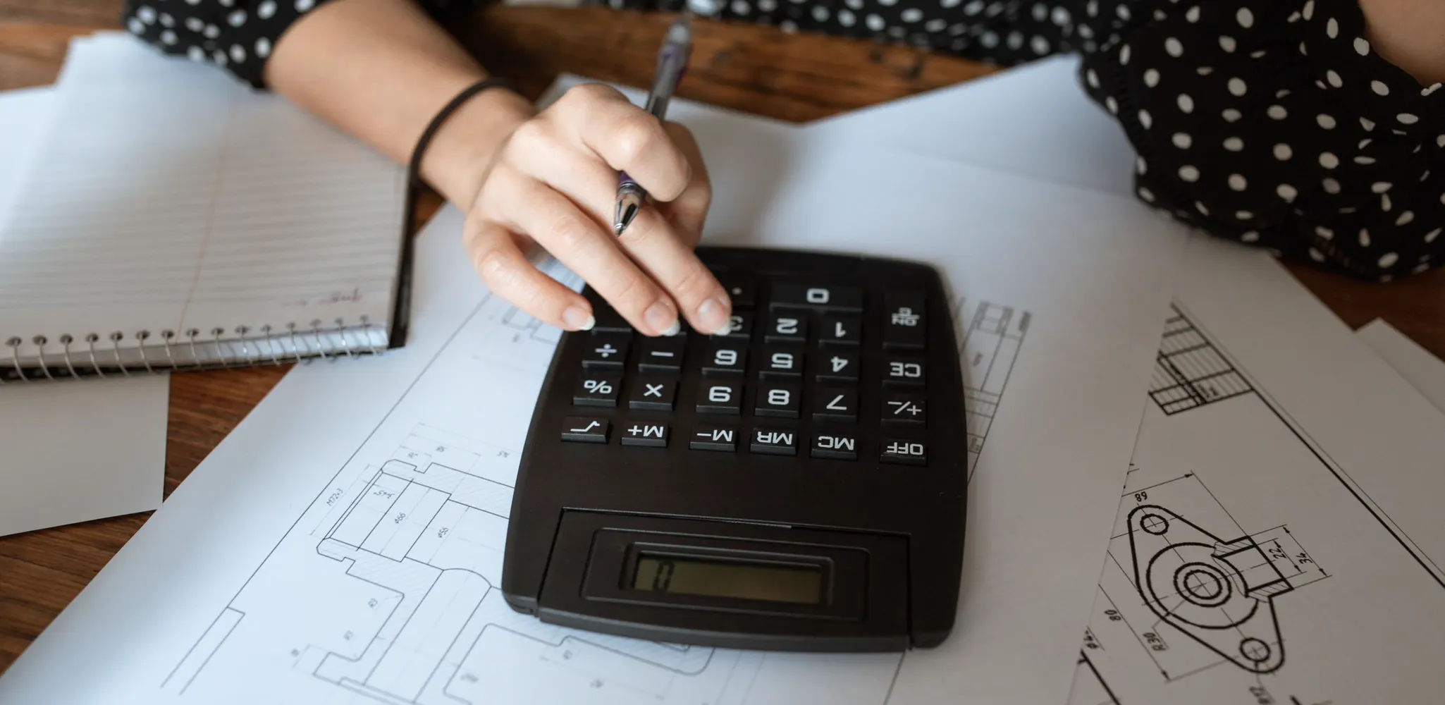A hand working a calculator over a set of building drawings, how we price remodeling work