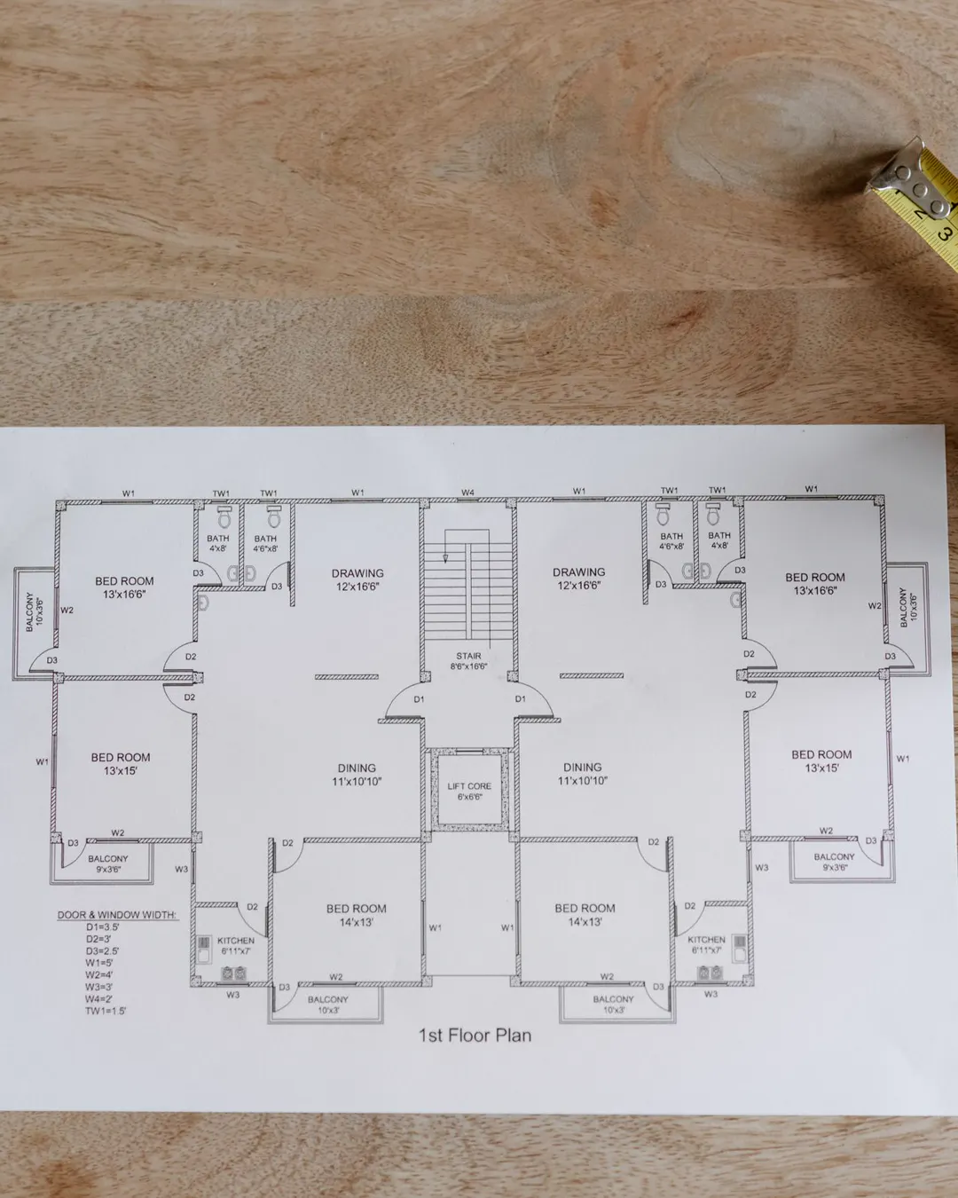 A floor plan on a wooden table with a tape measure, a pen and a cup of coffee, how we price a remodel