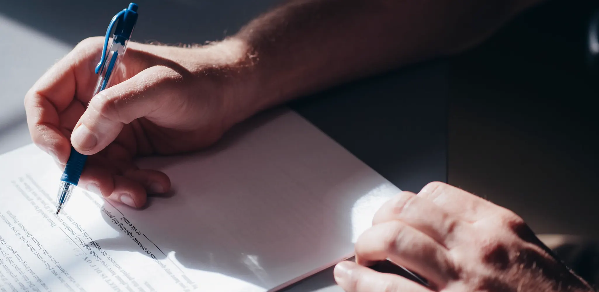 A hand signing a paper agreement with a blue pen, the legal page of Maplex Services