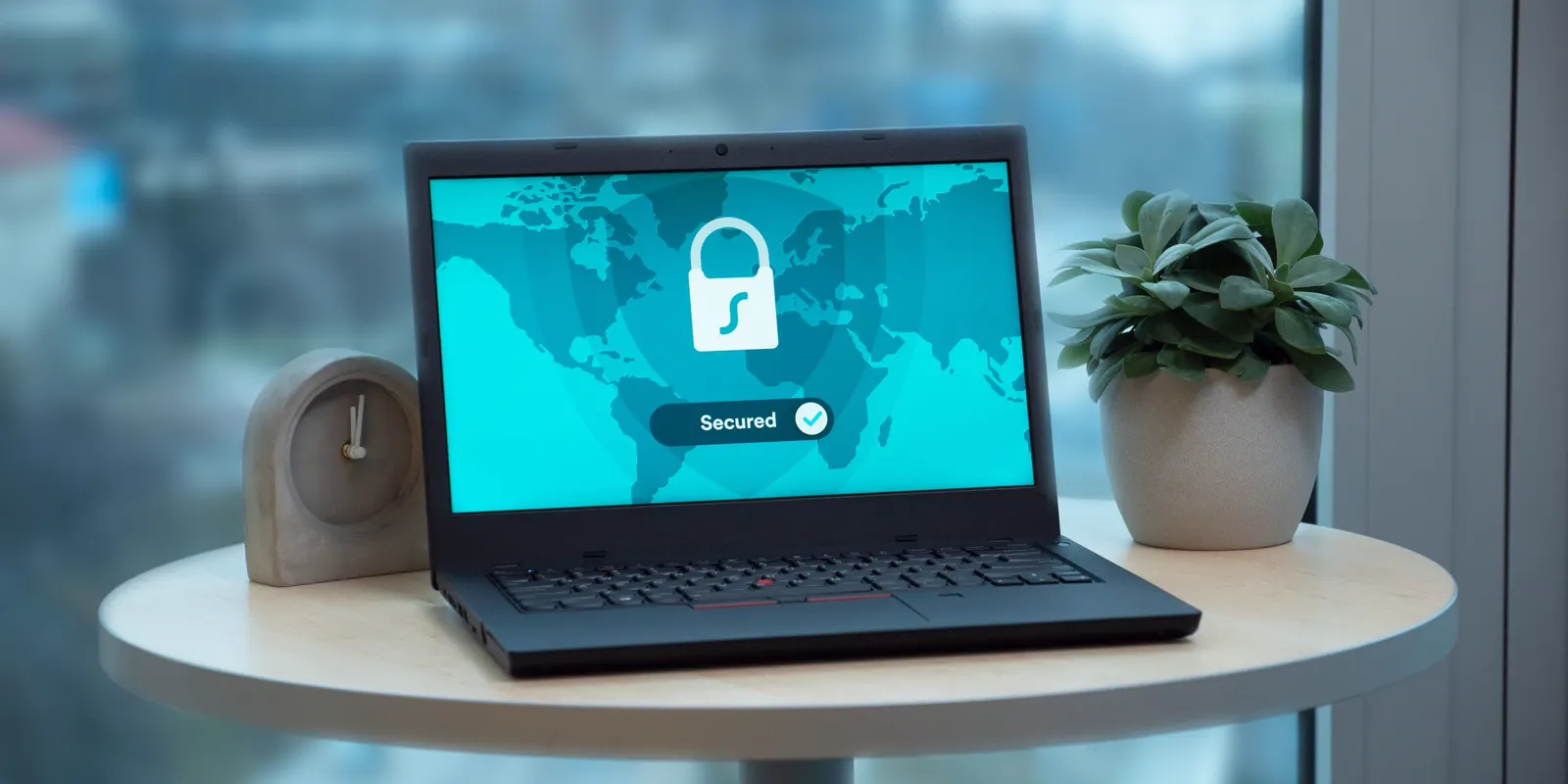A laptop on a table showing a padlock icon on its screen, next to a small plant