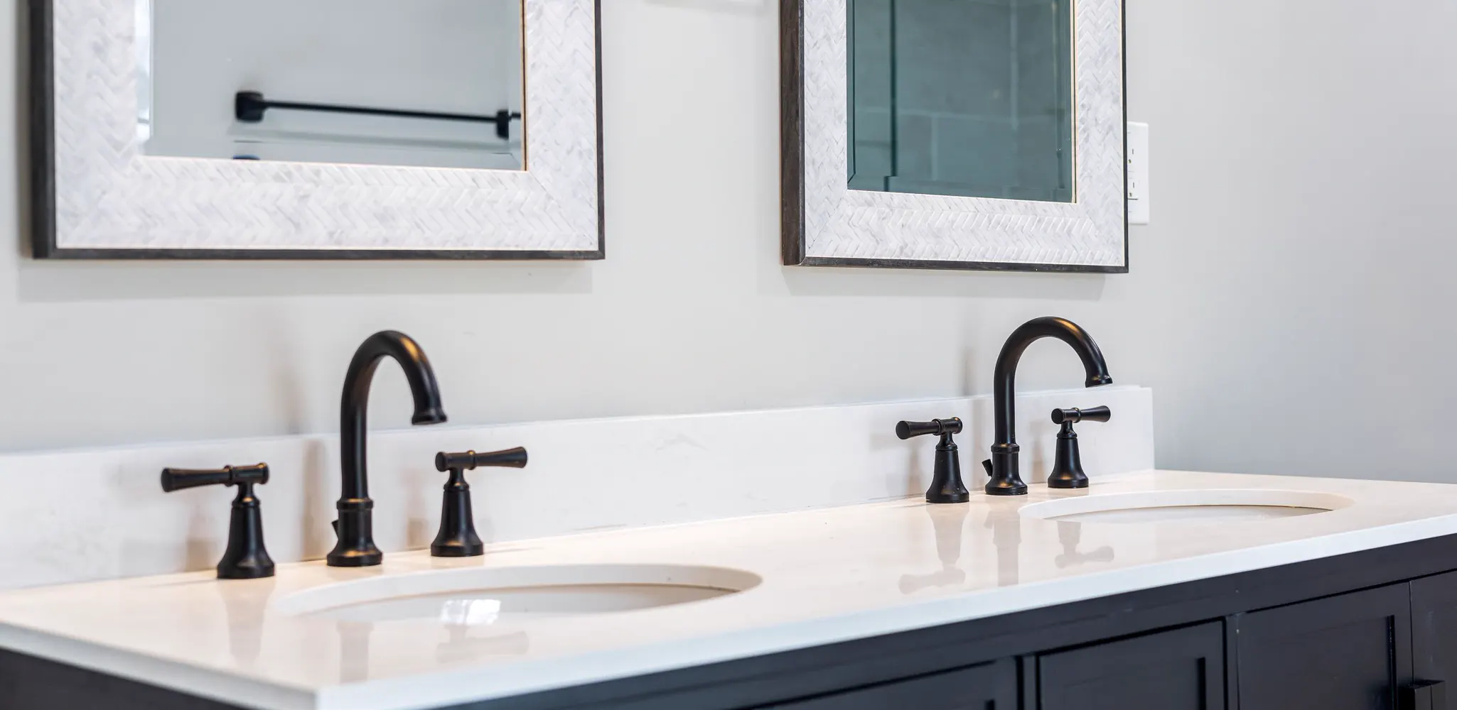 A bathroom vanity with two sinks and black faucets on a white top, the finished side of a vanity installation