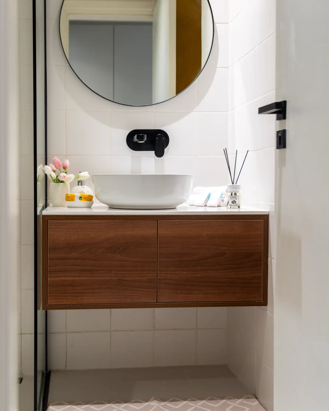 A bathroom with a round mirror, a vessel sink and a wooden vanity cabinet, bathroom vanity installation