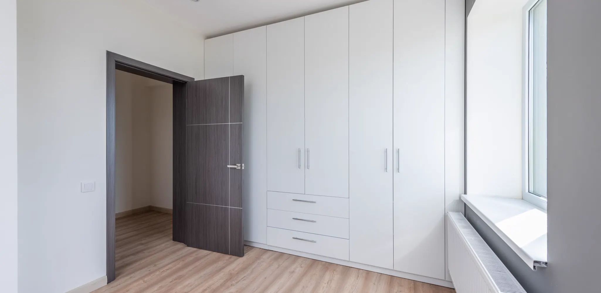 A bright empty room with new white cabinets and a wood floor, the finished side of a cabinet job