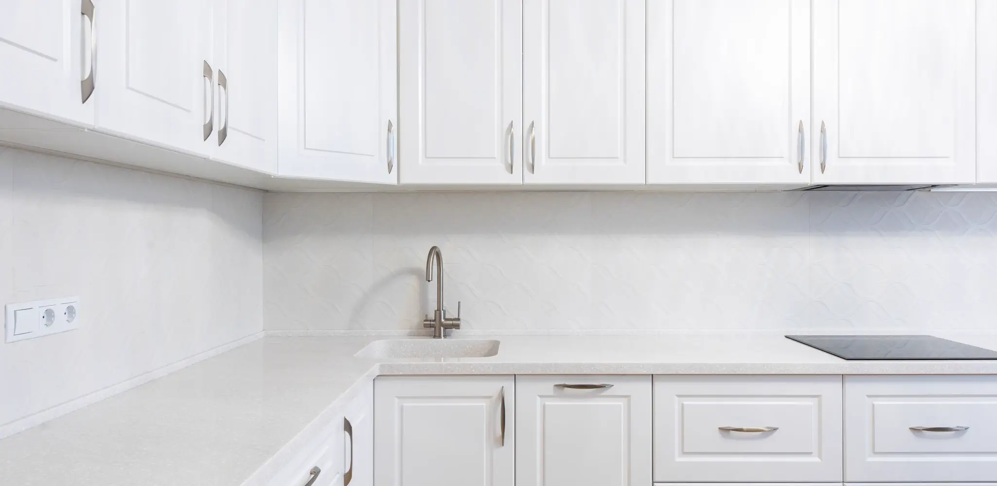 White cabinets around a sink and a cooktop under a hood, cabinet installation