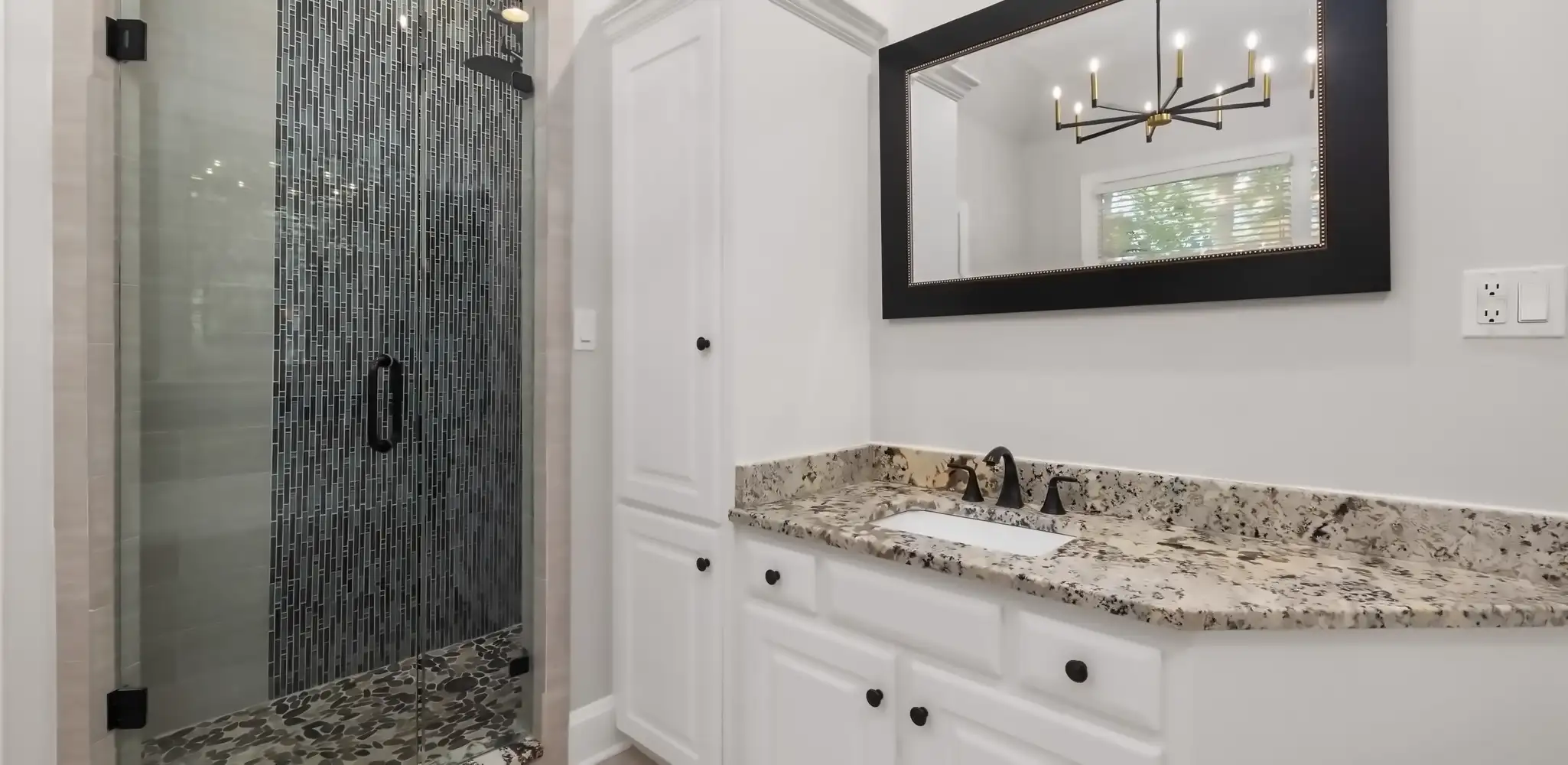 A bathroom vanity with a granite top and a tiled shower behind it, bathroom remodeling