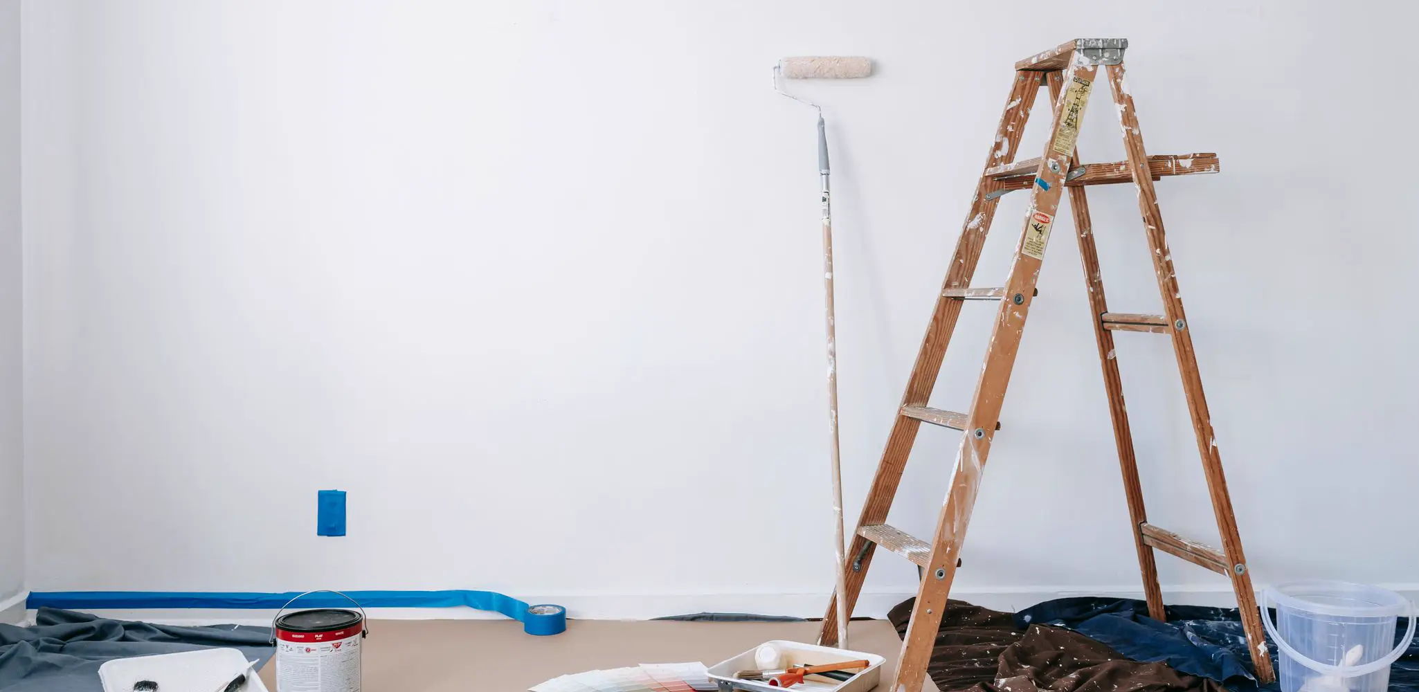 A room ready for paint, with a ladder, supplies and drop cloths, interior and exterior painting