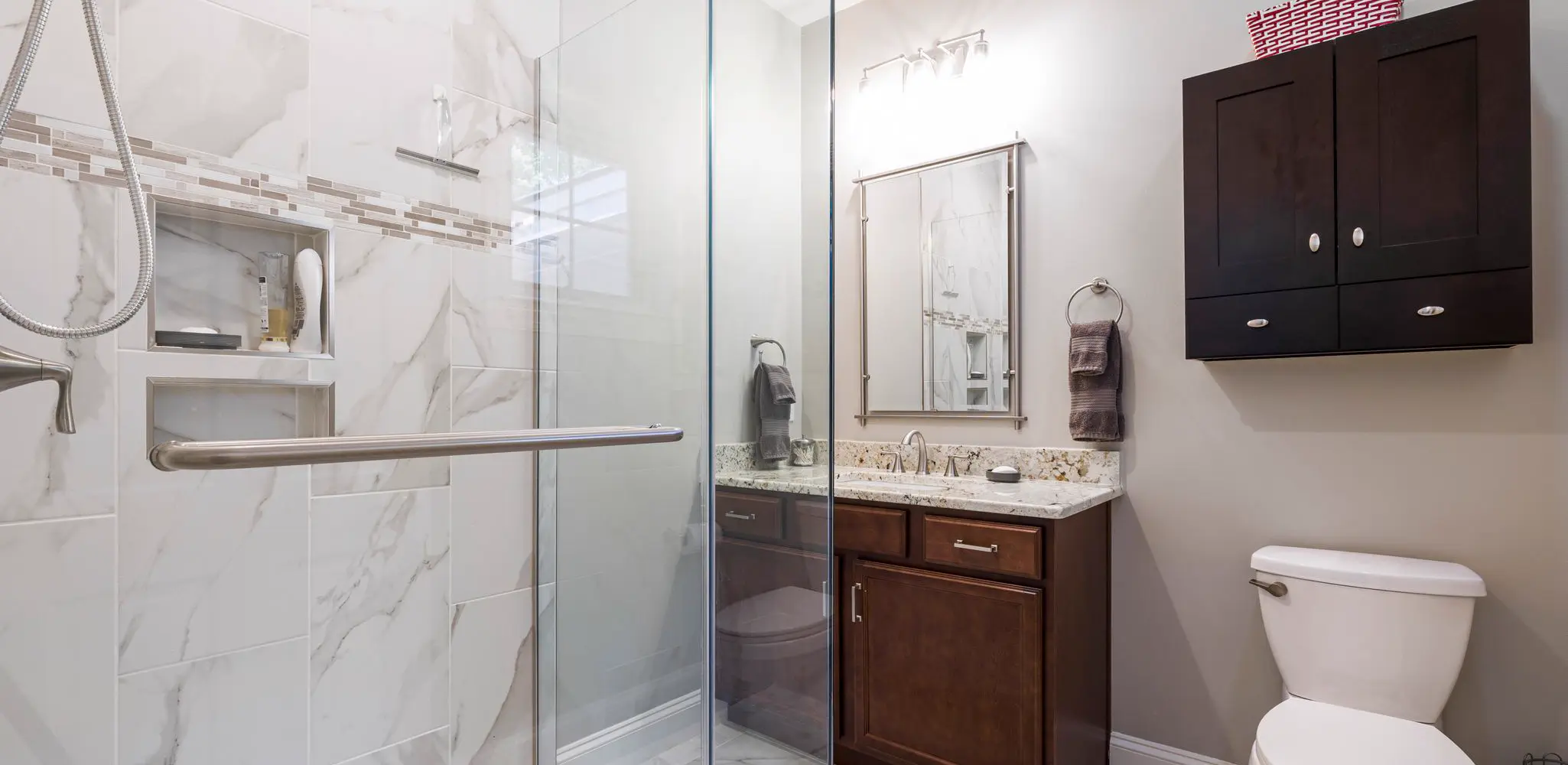A glass shower with marble tile and a dark wood vanity, bathroom remodeling