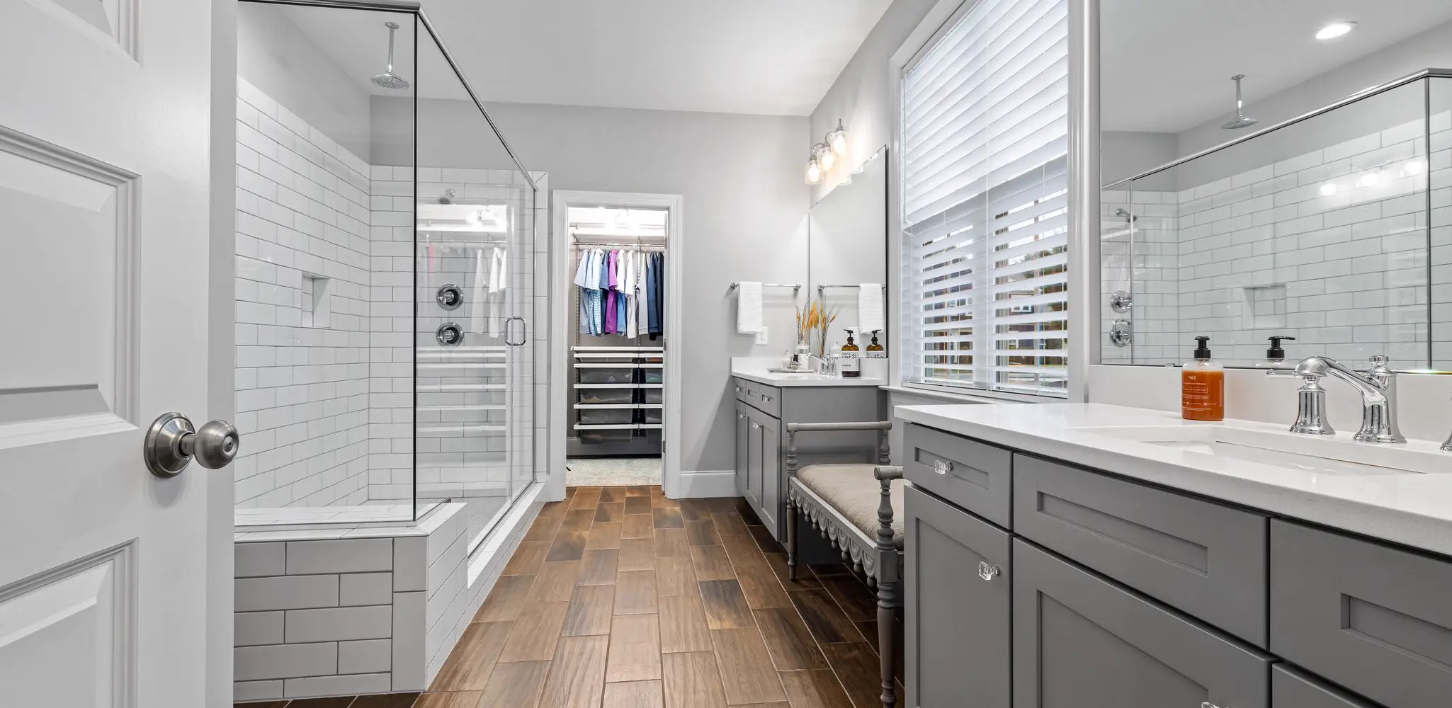A bathroom with a glass shower, wood floor and gray cabinets, bathroom remodeling