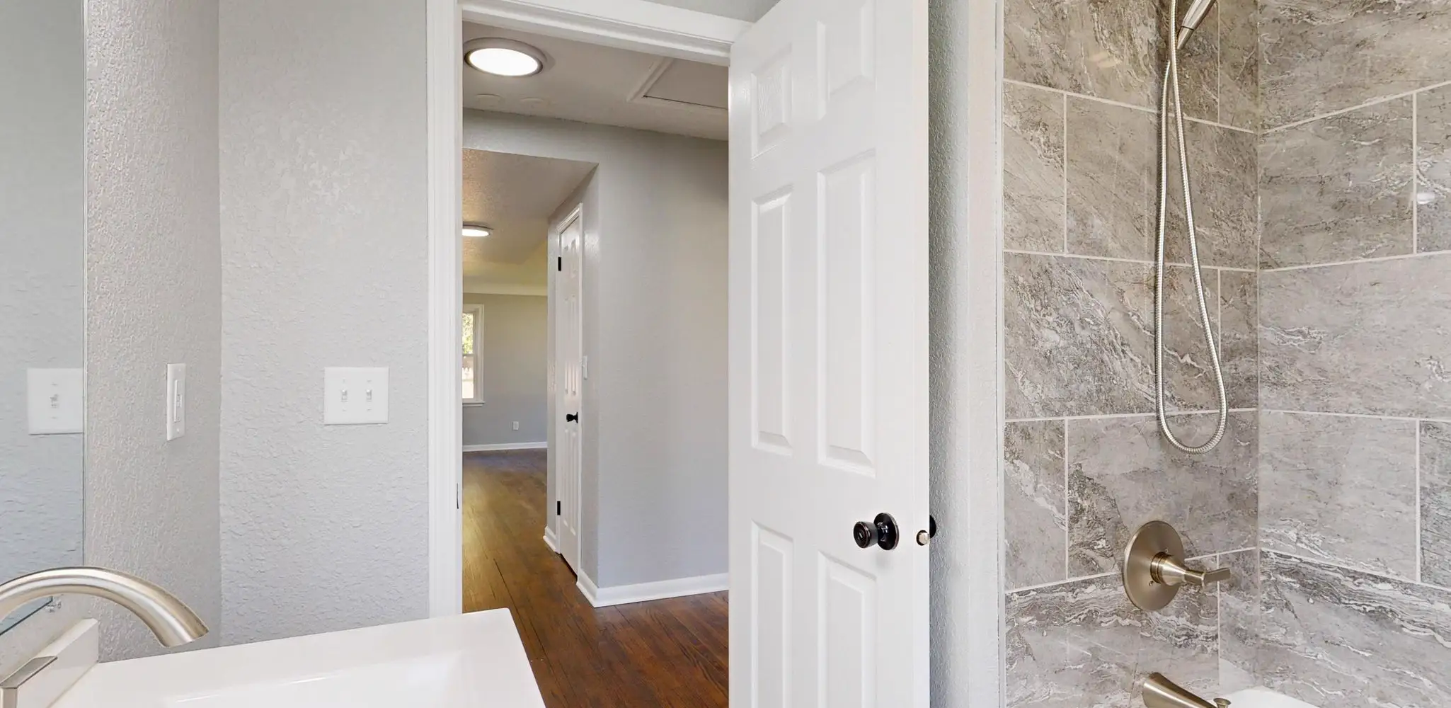 A gray tile shower with a glass door and black fixtures, bathroom remodeling