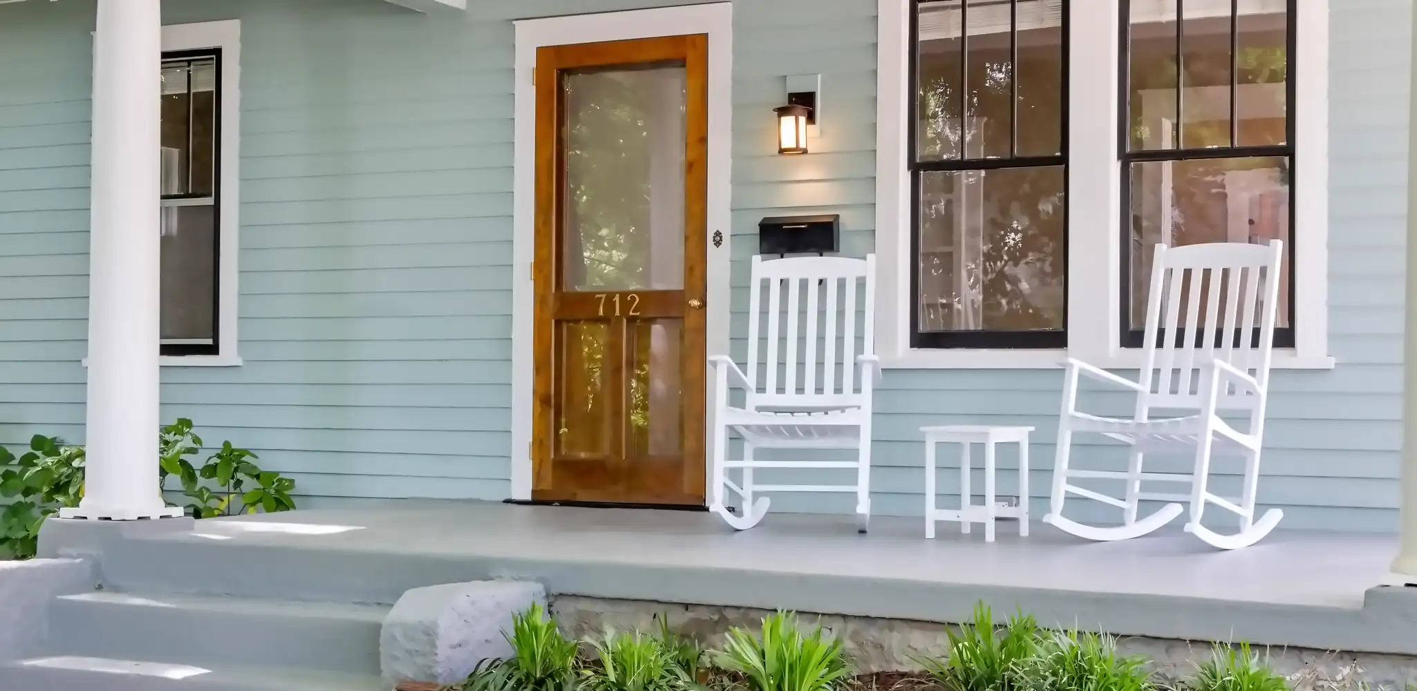 A front porch with white rocking chairs and a wood door, exterior and front of house