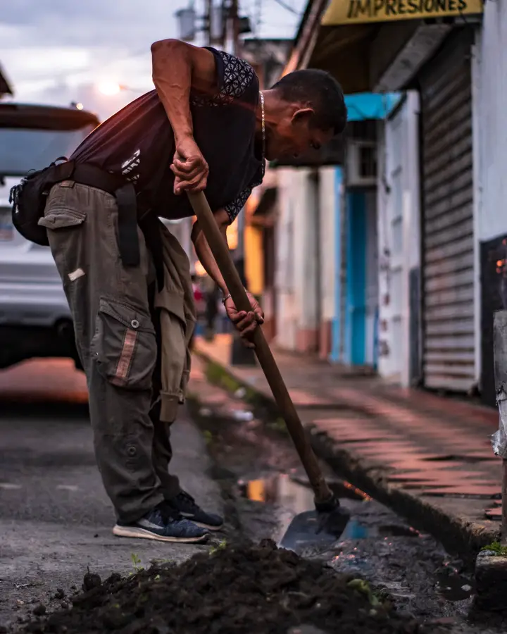 A worker with a shovel repairing a hole in a paved road, where a repair or a replacement gets decided