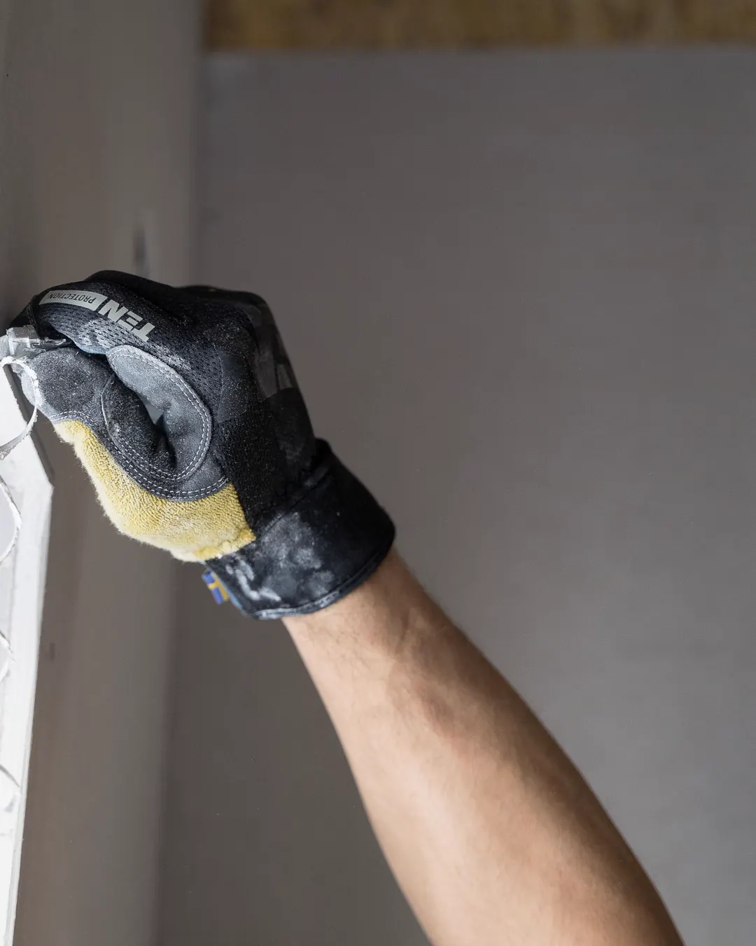A gloved hand smoothing compound on a drywall seam, drywall repair