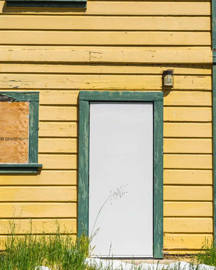 An older wooden house with peeling paint and a boarded window, where rot gets found before paint goes on