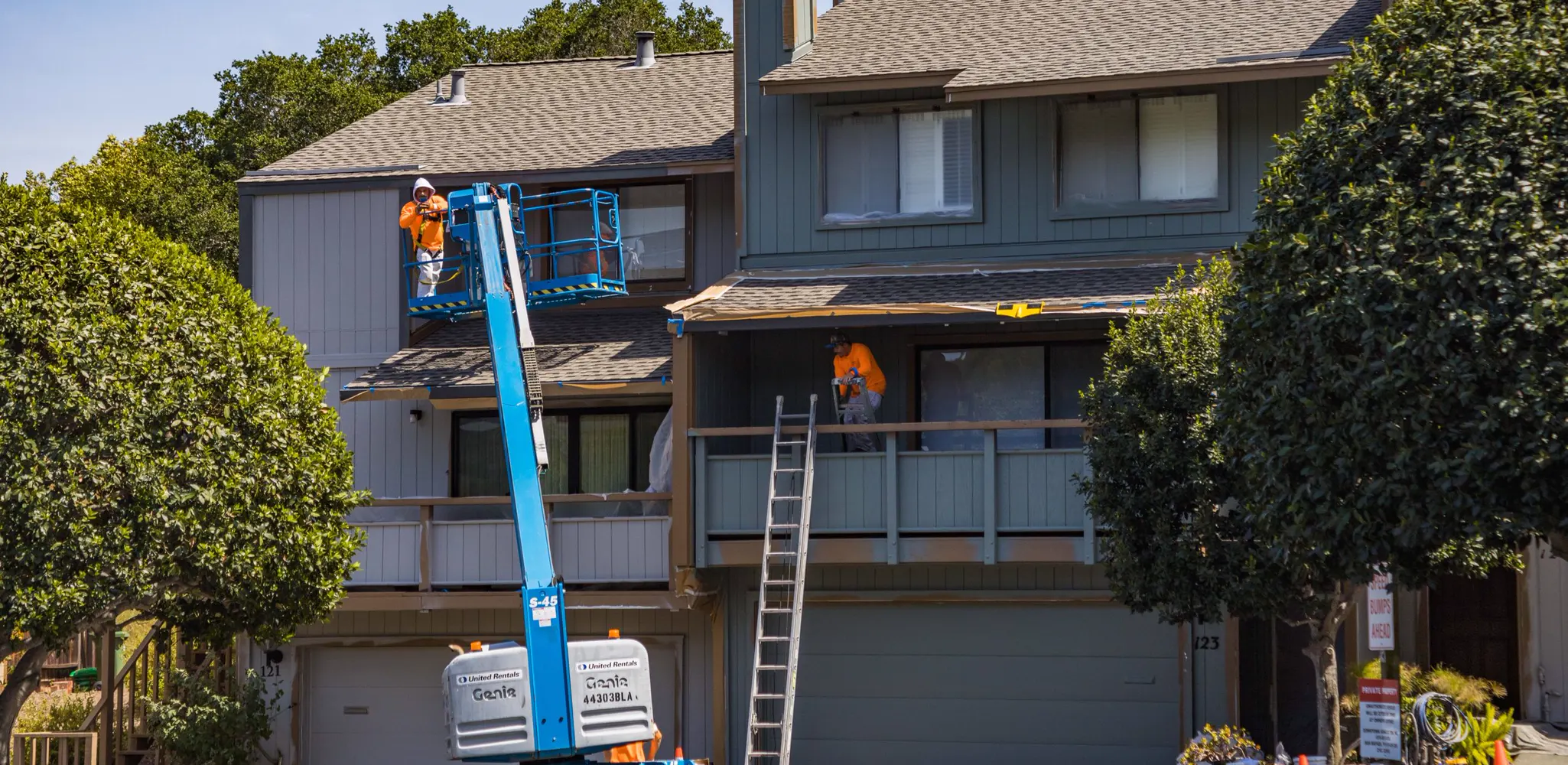 A lift and ladders set up against a two story house during exterior painting