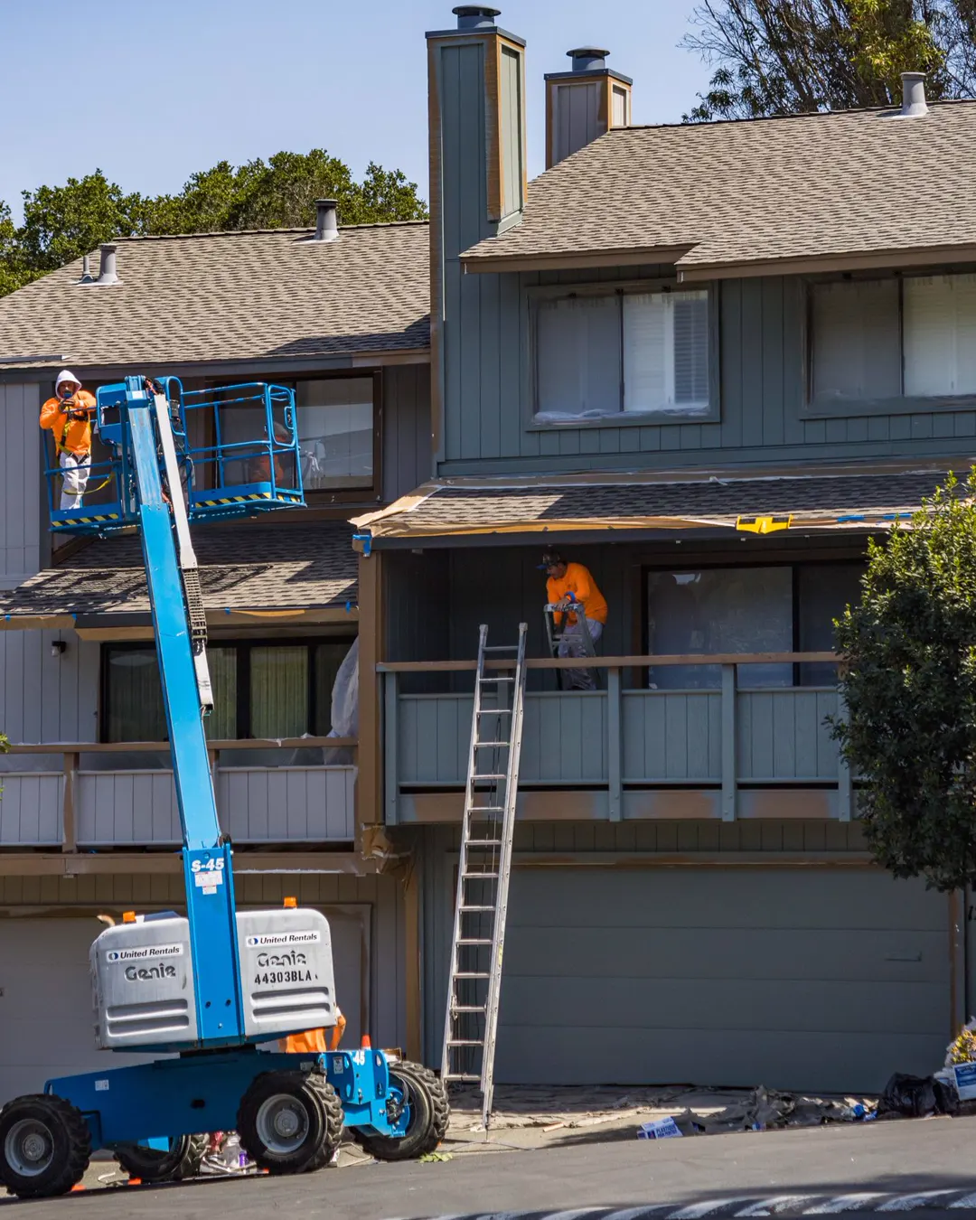 A painter on a lift working on the upper wall of a two story house, exterior painting