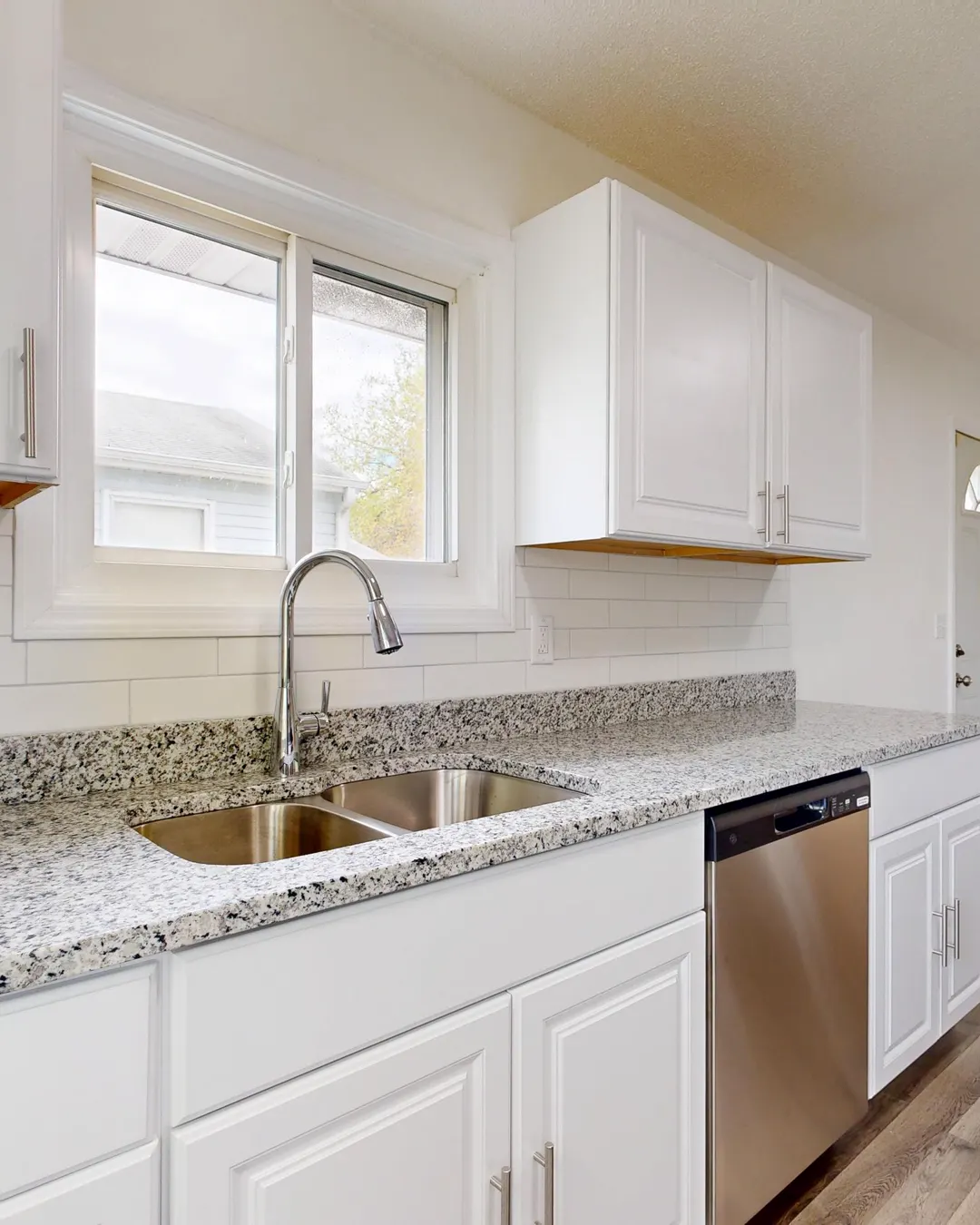 A white kitchen with wood look plank flooring and stainless appliances, new flooring cost