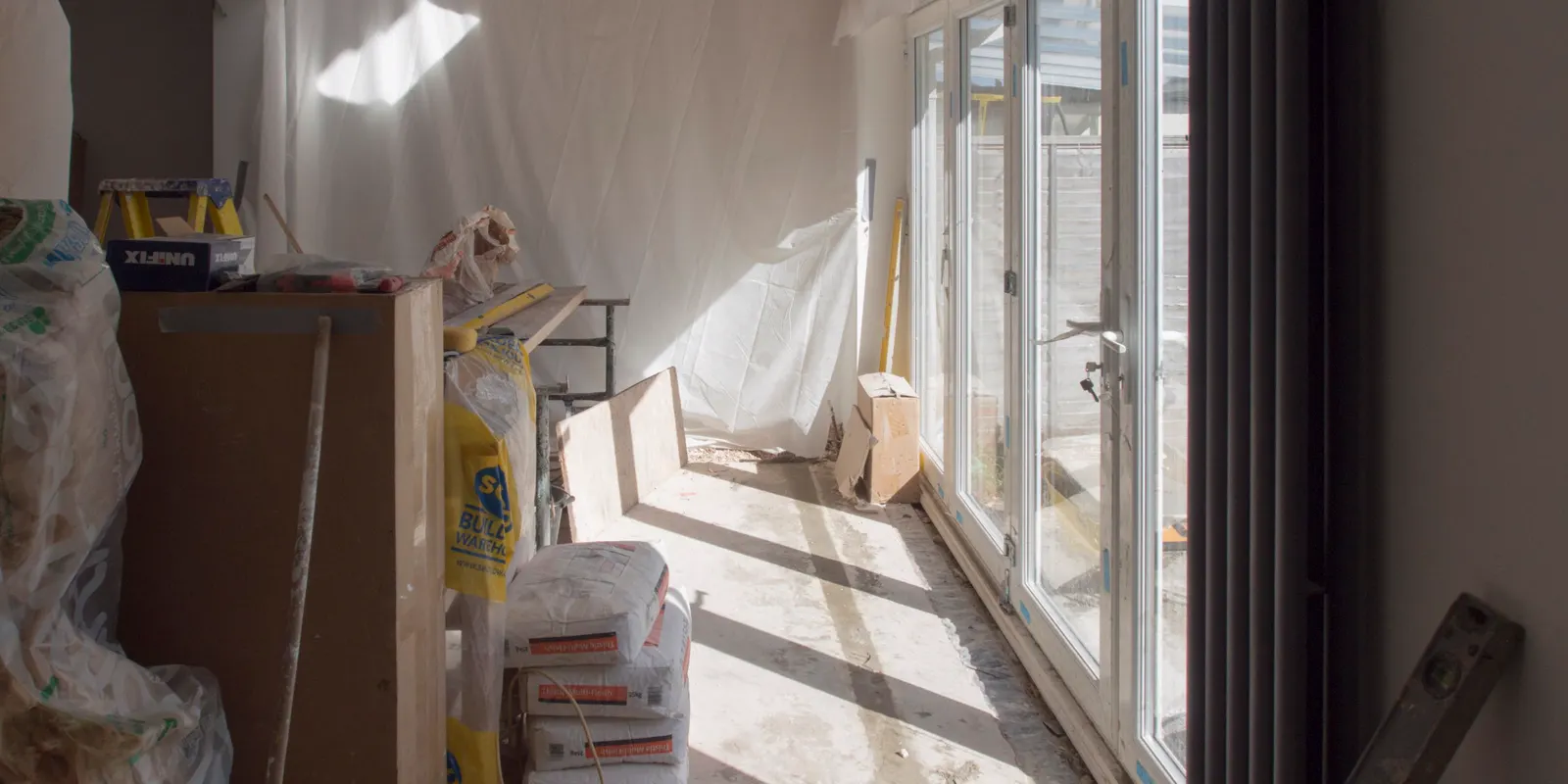 A room under renovation with plaster on the walls and materials on the floor, garage to apartment conversion