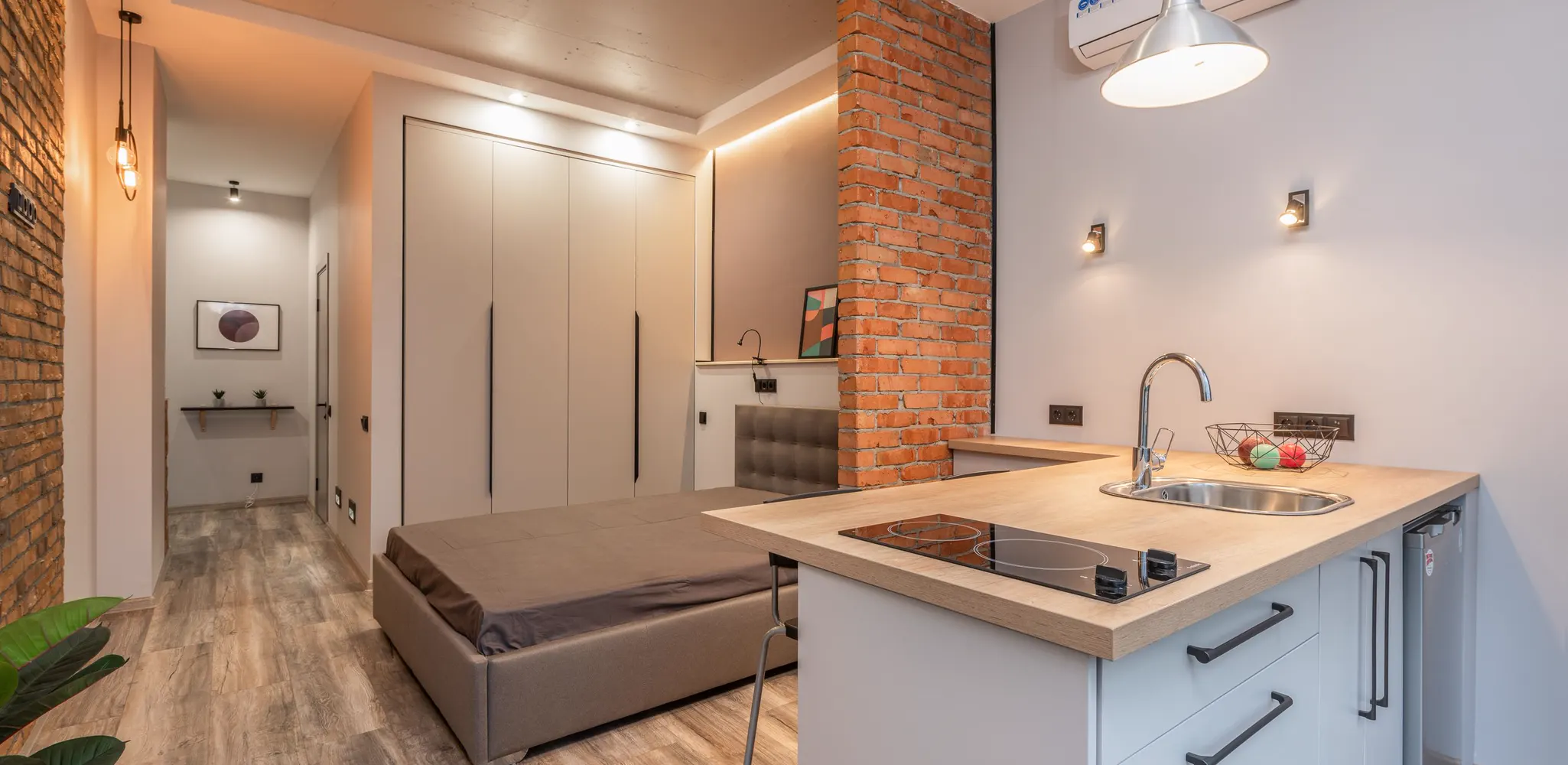 A small studio with a kitchen counter and a bed behind a brick wall, garage to apartment conversion