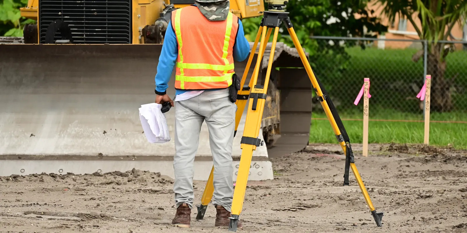 A surveyor seen from behind taking measurements on a construction site, home addition cost