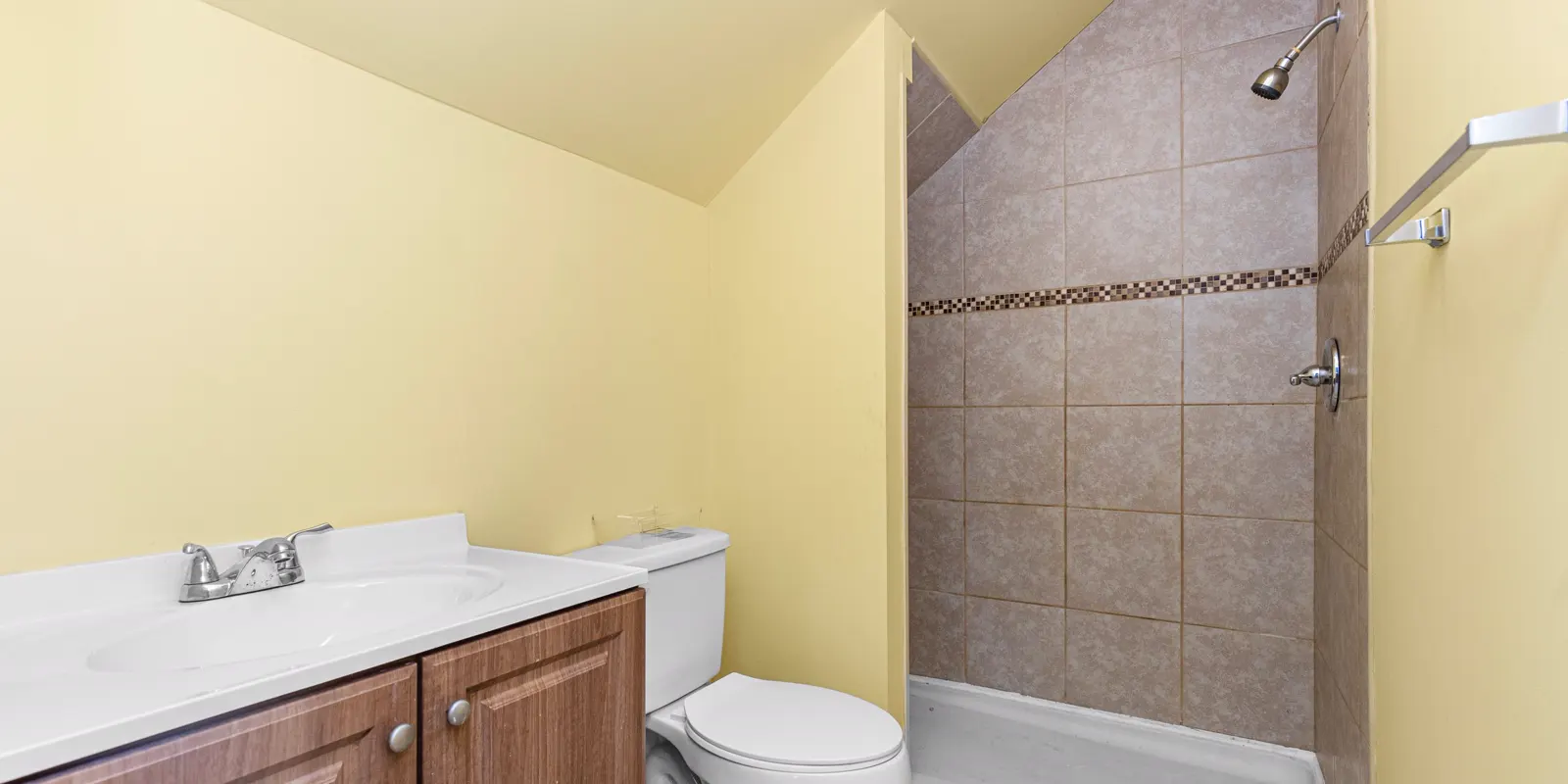 A small bathroom with a walk in shower, a grab bar and a wood vanity, in-law suite conversion