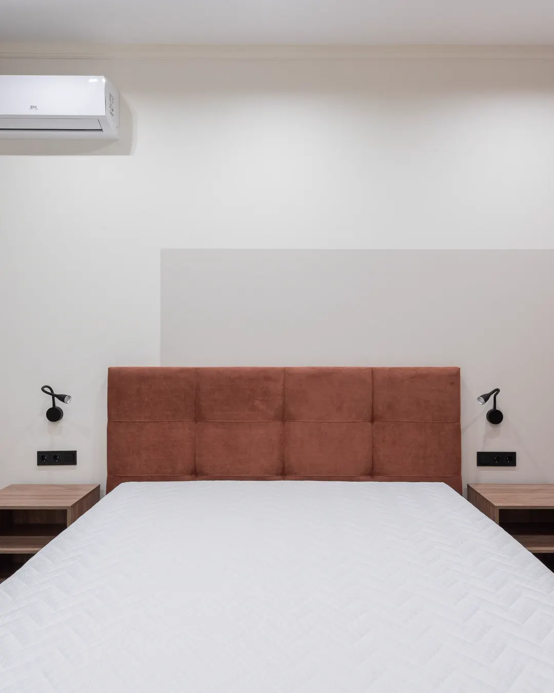 A compact bedroom with a bed, two small lamps and a wall air conditioner, in-law suite conversion