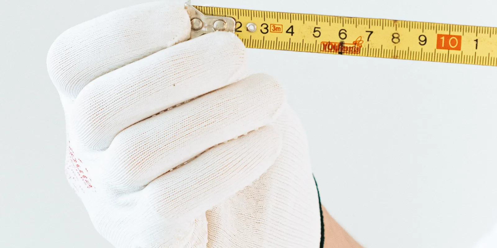A gloved hand holding a tape measure against a wall, interior door replacement