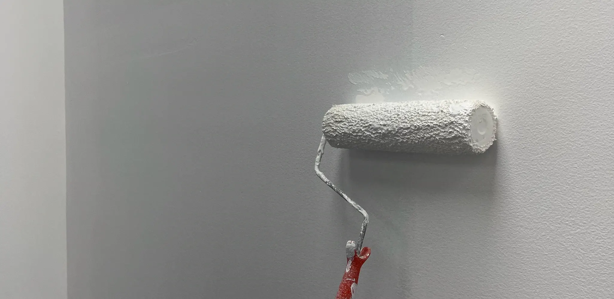 Fresh white paint being rolled onto an interior wall, interior painting