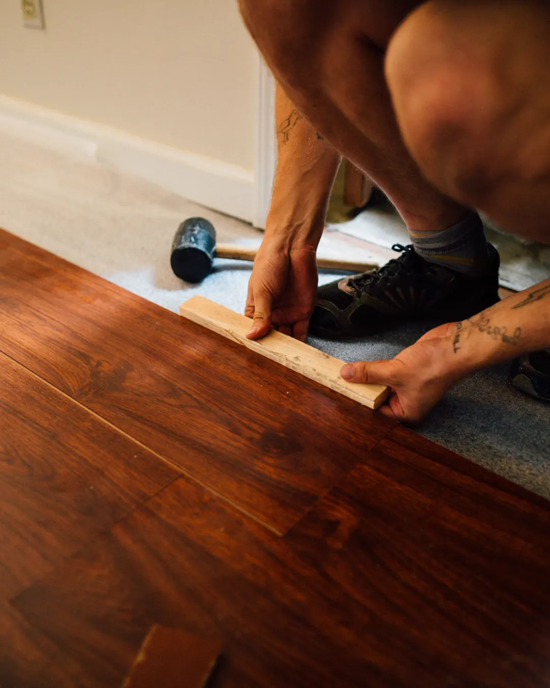 Laminate planks being tapped together with a mallet and a tapping block, laminate flooring installation