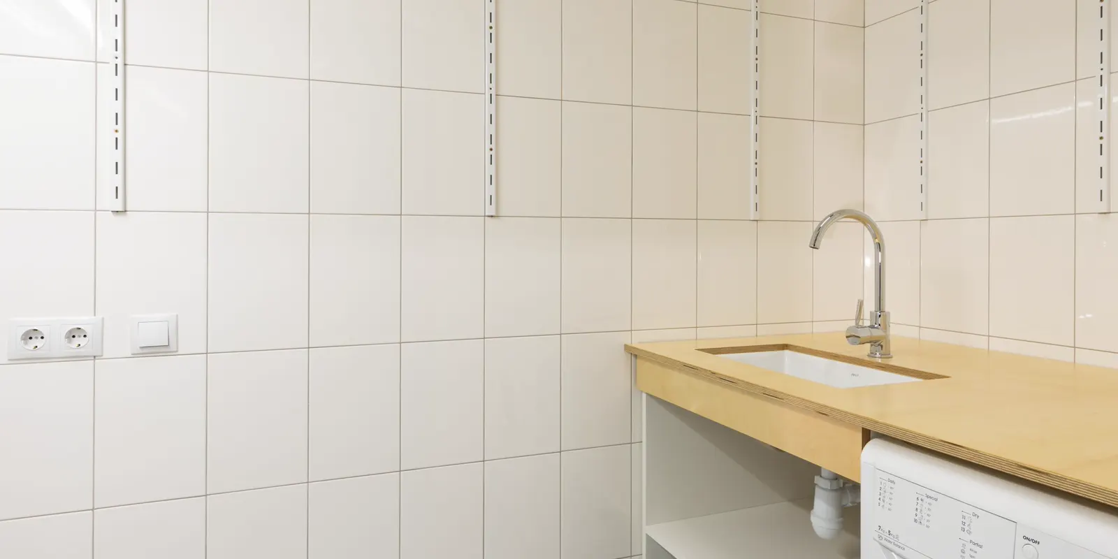A laundry room with a washer, a sink and open shelving, laundry and garage cabinets
