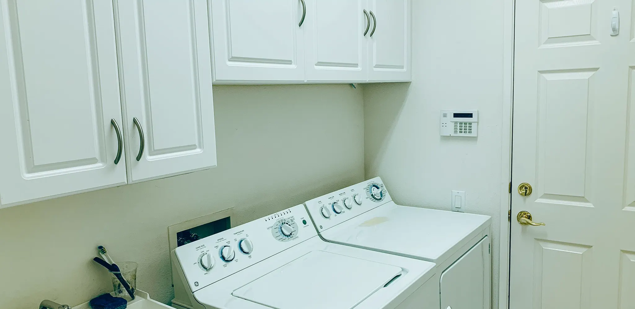A laundry room with white cabinets over a washer and a dryer, the finished side of a laundry cabinet job