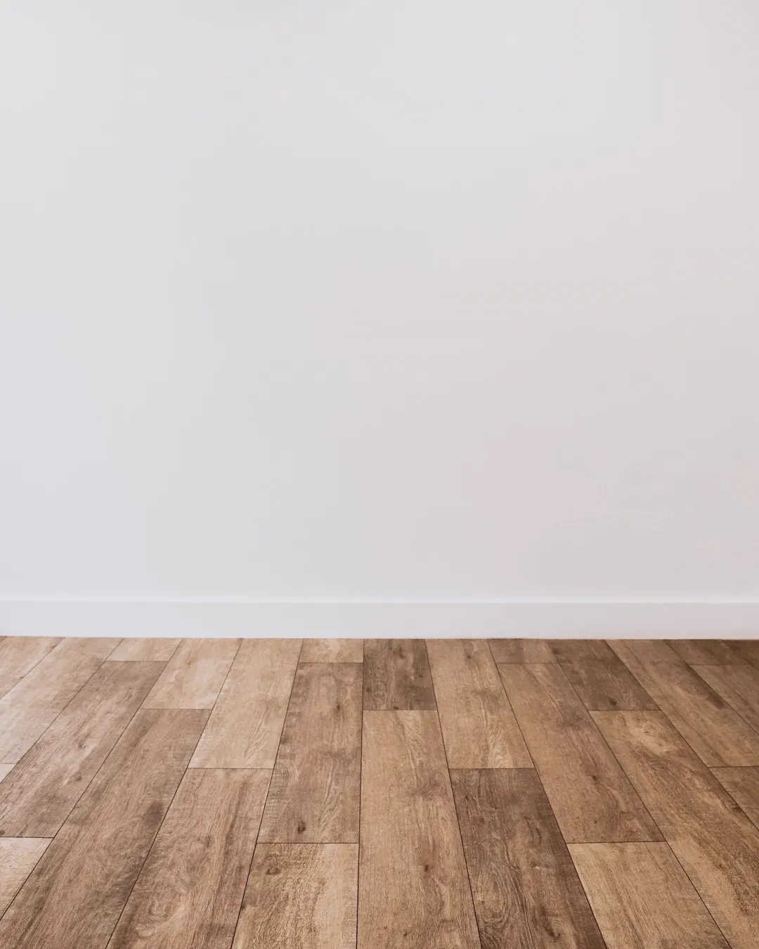 Wood look vinyl plank flooring meeting a white wall and baseboard, luxury vinyl plank