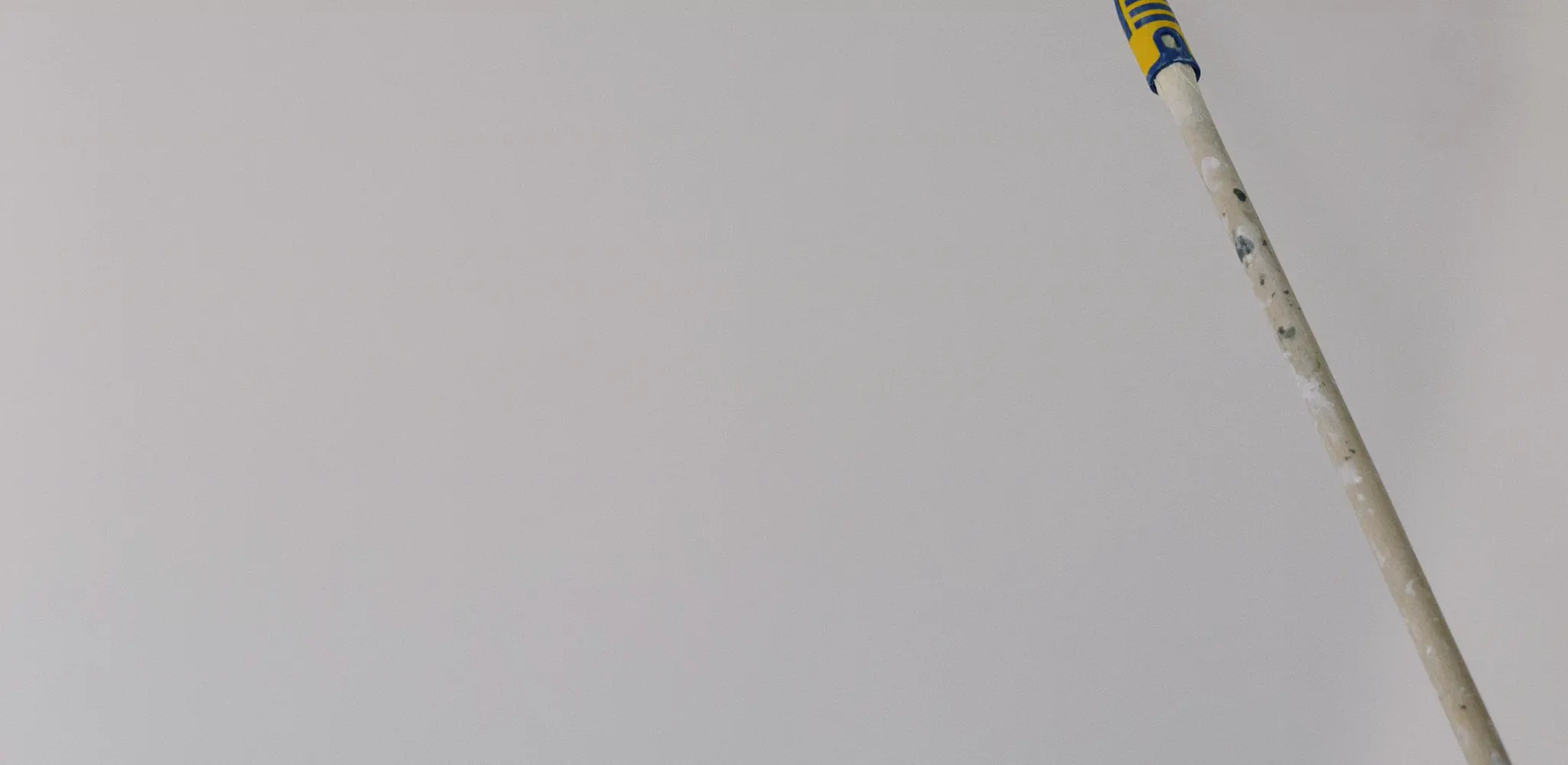 Paint roller on a pole rolling a white wall, house painting cost