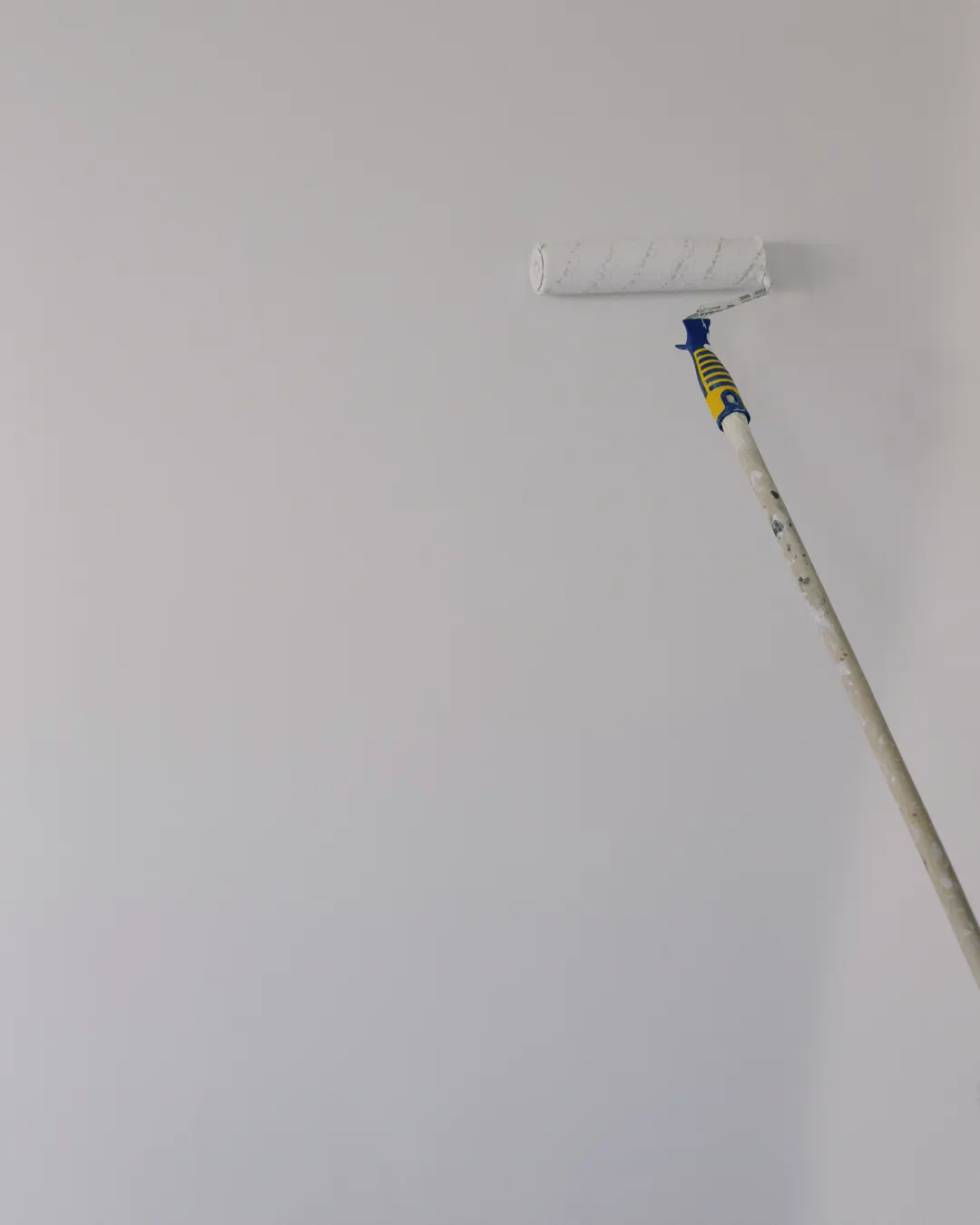 A paint roller on an extension pole against a freshly painted white wall, house painting cost