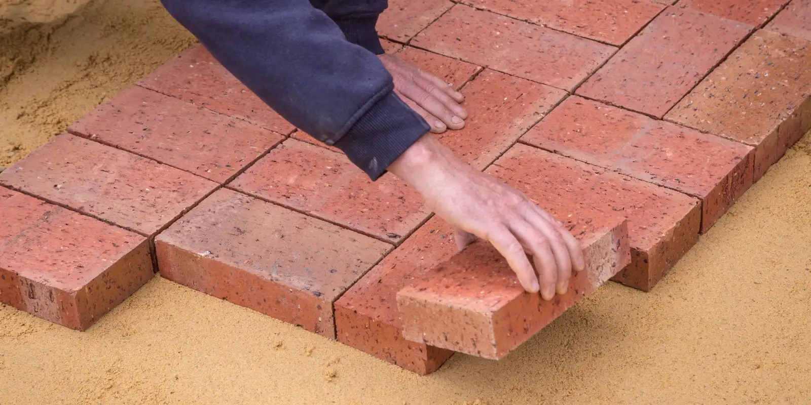 A worker seen from above laying paving stones on a sand bed, paver driveway