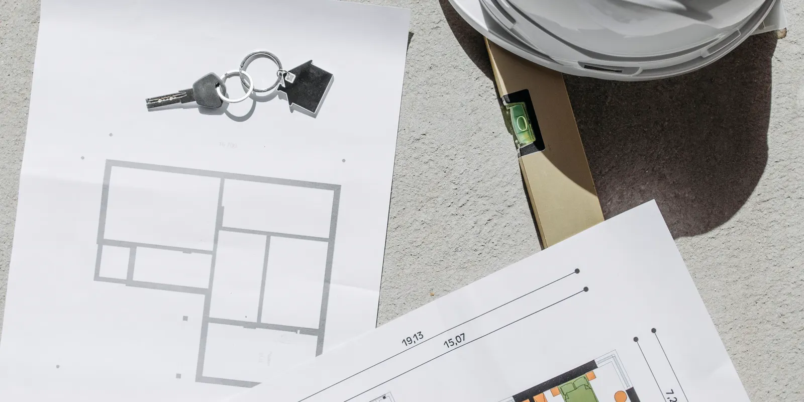 Construction plans, keys, a hard hat and a level laid out on concrete, room addition