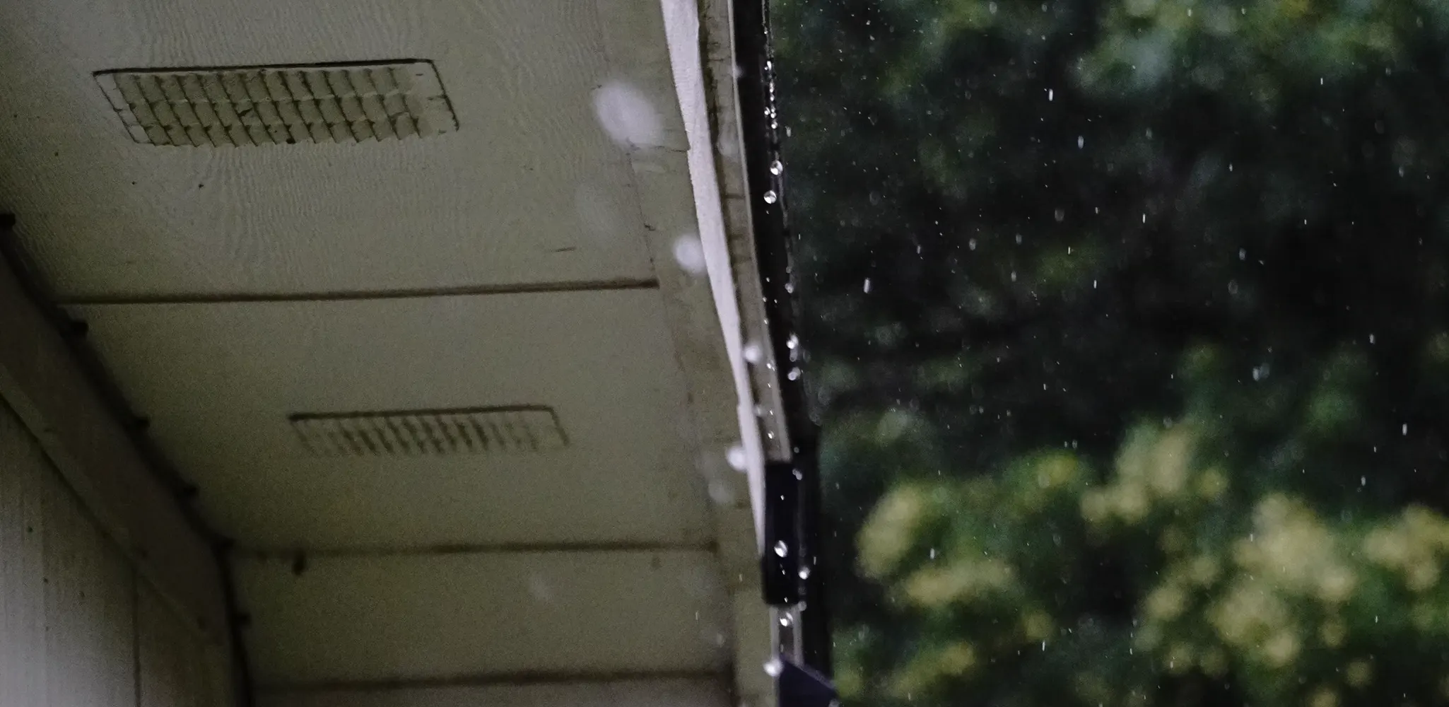 Vented soffit panels under a roof edge with rain falling, soffit and fascia repair