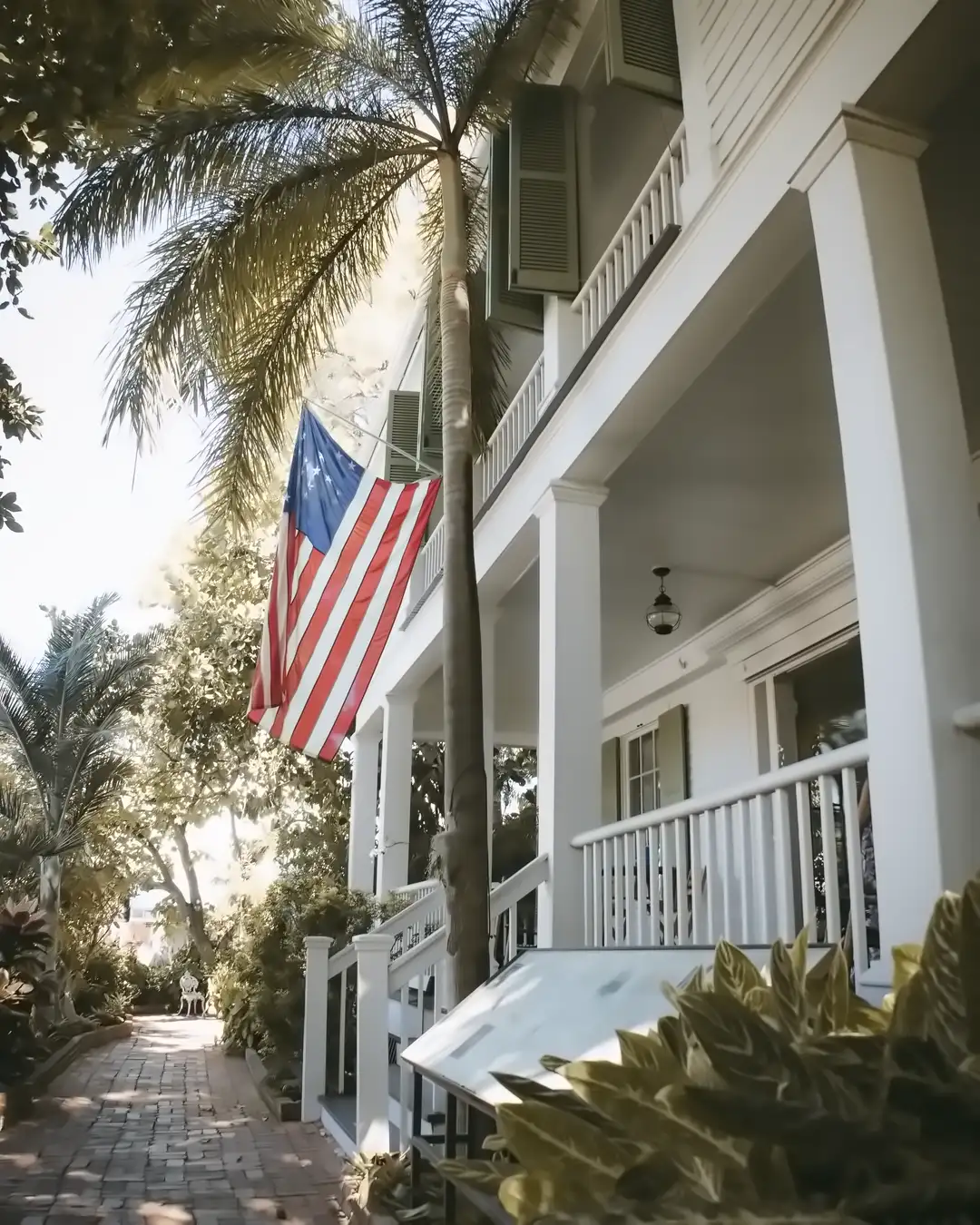 A white wood porch with shutters, a flag and a palm over a brick walk, the kind of house home remodeling in St. Petersburg, FL often starts with