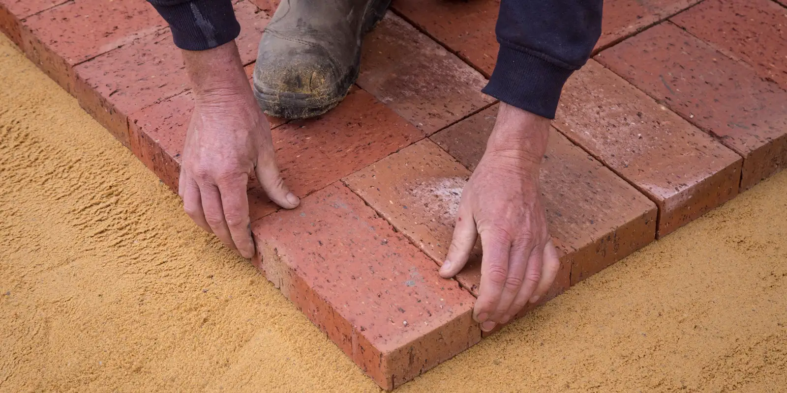 A worker seen from above setting pavers on a walkway base, sidewalk repair